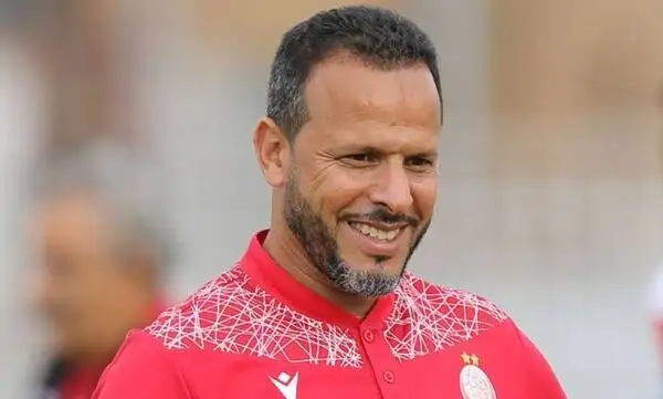 koo_459622jpg | MCG24 | موقع إلكتروني مغربي شامل متجدد على مدار الساعة Smiling man in a red sports jersey with a white geometric pattern on the shoulders, outdoor blurred background.