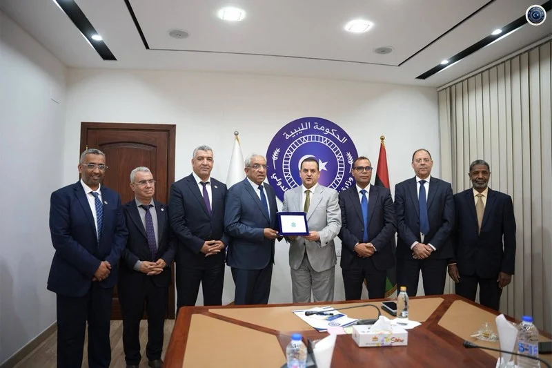 libye-comite-parlementaire-marocain-1 | MCG24 | موقع إلكتروني مغربي شامل متجدد على مدار الساعة Group of men in suits posing for a formal award ceremony, central figure holding a plaque, emblem backdrop with Arabic text behind them.