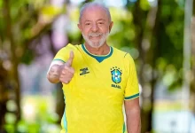 Smiling older man in a Brazil national team jersey giving a thumbs up outdoors.