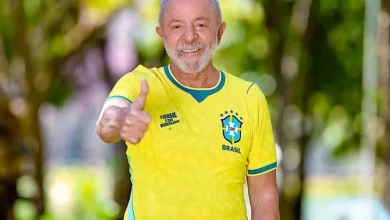 Smiling older man in a Brazil national team jersey giving a thumbs up outdoors.