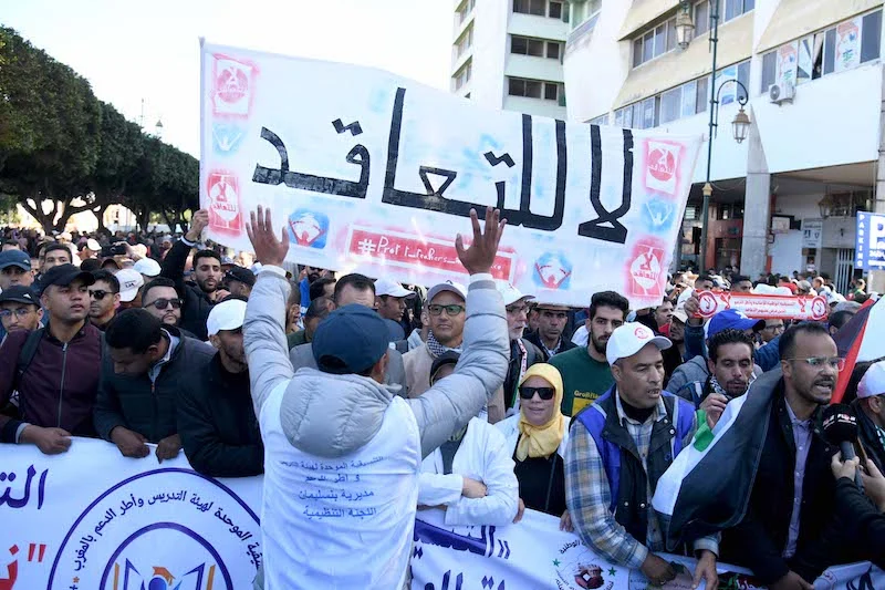 marche-enseignants-rabat32 | MCG24 | موقع إلكتروني مغربي شامل متجدد على مدار الساعة Crowd of protesters in a city street holding a large Arabic banner and smaller signs.