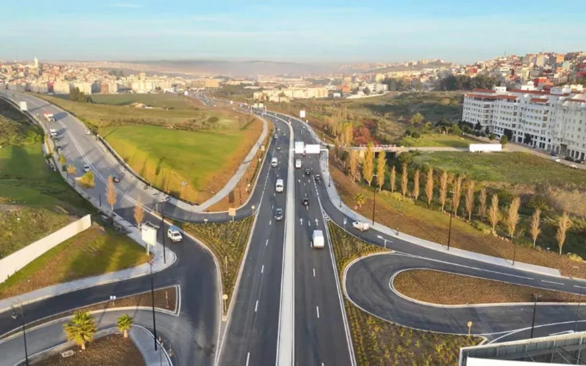 maroc-infrastructures-investissements-budget-ae832 | MCG24 | موقع إلكتروني مغربي شامل متجدد على مدار الساعة Aerial view of a multi-lane highway interchange with looping ramps, green fields on the sides and a city in the distance.
