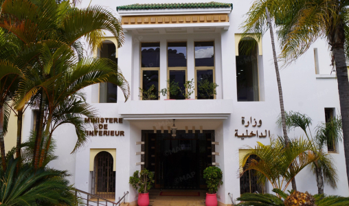 ministre-de-lInt-C3-A9rieur_png_jpg-1jpg-1jpg-1jpg-1jpg-1jpg | MCG24 | موقع إلكتروني مغربي شامل متجدد على مدار الساعة White colonial-style government building with arched entrance, French and Arabic signage reading 'Ministère de l'Intérieur', flanked by palm trees.