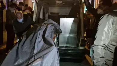 nador-mort2 | MCG24 | موقع إلكتروني مغربي شامل متجدد على مدار الساعة People wearing masks load a body covered by a gray tarp into a van at night, while bystanders watch nearby.