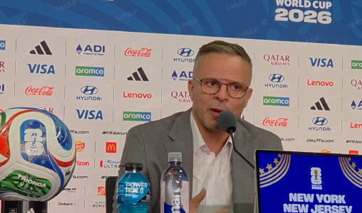 ouahbi-2 | MCG24 | موقع إلكتروني مغربي شامل متجدد على مدار الساعة Man in a suit and glasses speaks into a microphone at a press conference with a World Cup 2026 backdrop and sponsor logos behind him.