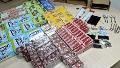 police | MCG24 | موقع إلكتروني مغربي شامل متجدد على مدار الساعة Assorted boxed products arranged in rows on a table, with blue, red, yellow packaging, plus several mobile devices, coins, and a few spoons and knives visible on the right.