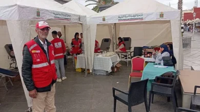sang-4 | MCG24 | موقع إلكتروني مغربي شامل متجدد على مدار الساعة Outdoor medical aid tents with volunteers in red vests; a man wearing a red cap stands in foreground while others assist at tables under white canopies