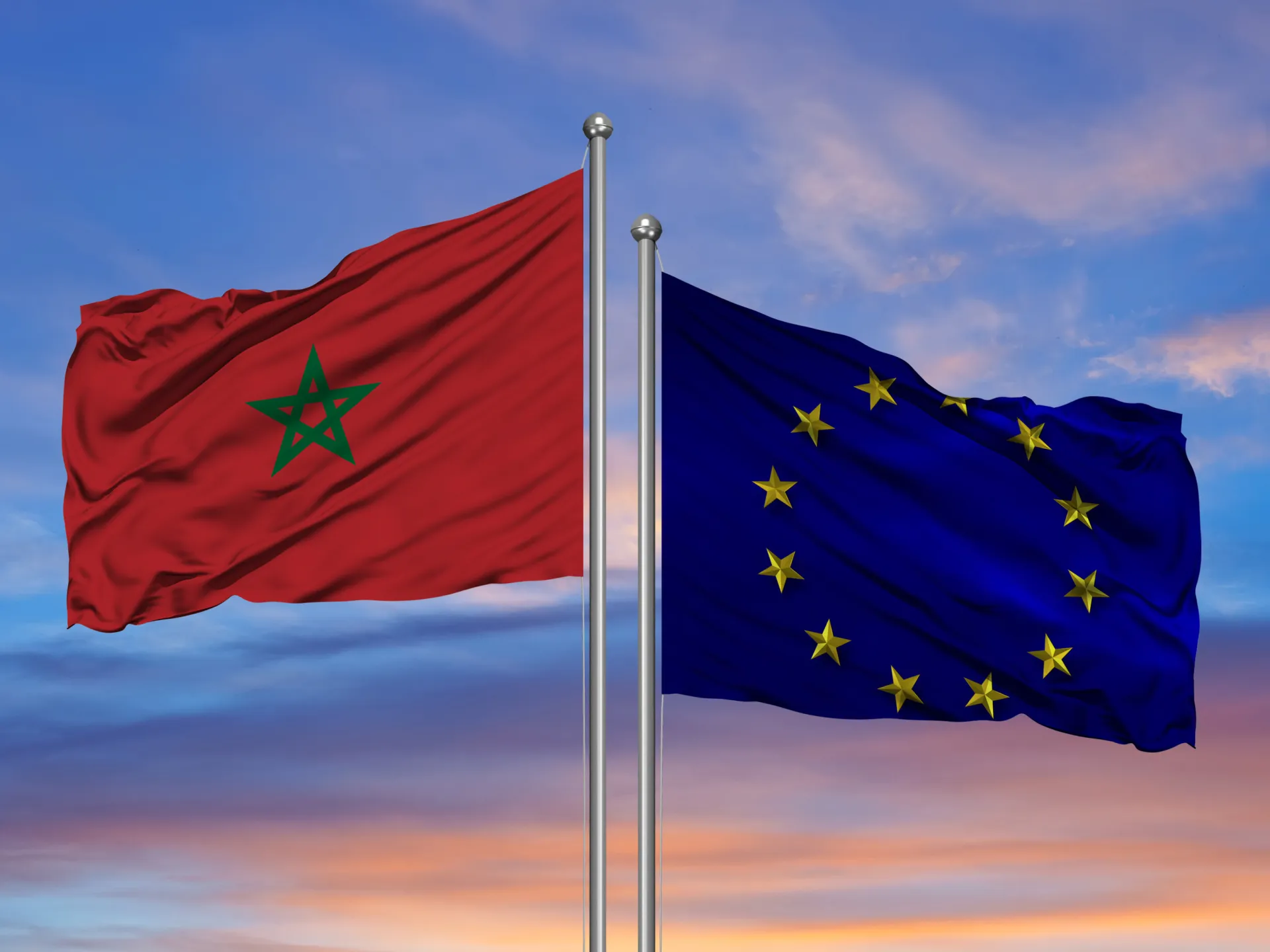 sgsqgsfdg3-1739014574 | MCG24 | موقع إلكتروني مغربي شامل متجدد على مدار الساعة Moroccan flag with green five-pointed star waving beside the European Union flag on flagpoles at sunset.