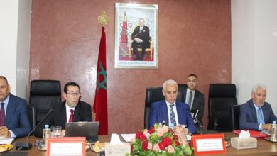 srm-fes-1ere-annee-800 | MCG24 | موقع إلكتروني مغربي شامل متجدد على مدار الساعة Group of men in suits sit at a conference table in a formal meeting room, with a Moroccan flag and a framed portrait on the wall behind them.