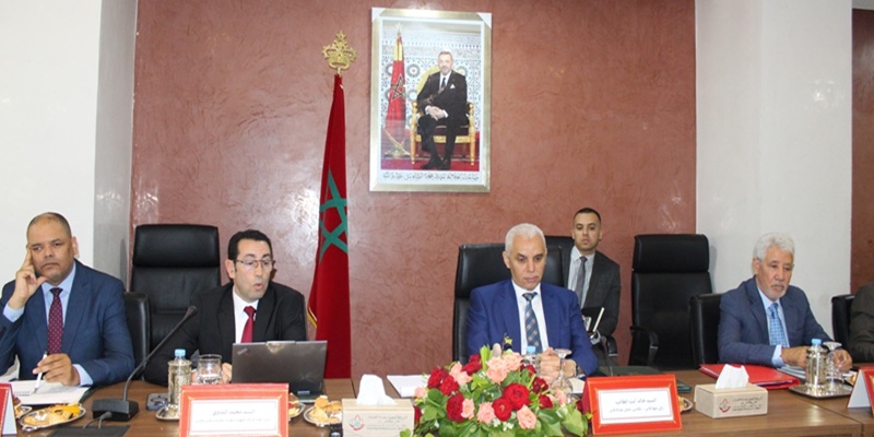 srm-fes-1ere-annee-800 | MCG24 | موقع إلكتروني مغربي شامل متجدد على مدار الساعة Group of men in suits sit at a conference table in a formal meeting room, with a Moroccan flag and a framed portrait on the wall behind them.