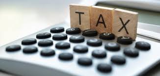 Calculator with wooden tiles spelling TAX resting on top, conveying a tax concept