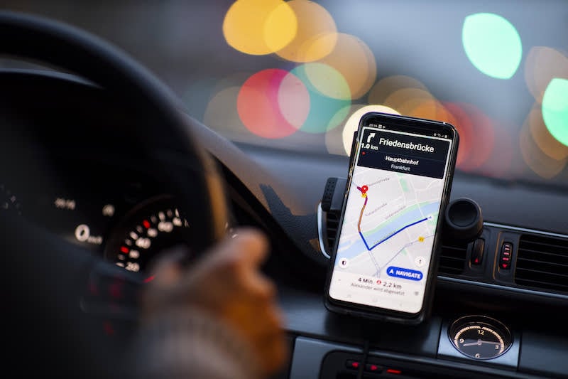 transport-application | MCG24 | موقع إلكتروني مغربي شامل متجدد على مدار الساعة Phone mounted on a car dashboard displaying a navigation app with a route on a map in focus, city lights blurred in the background.