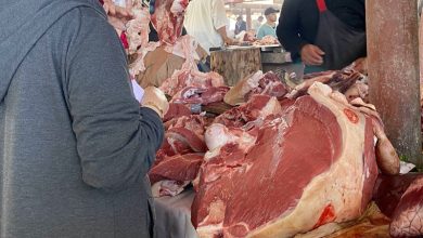 viande-2 | MCG24 | موقع إلكتروني مغربي شامل متجدد على مدار الساعة Meat market stall with large cuts of beef on a table; a customer in a gray hoodie selects meat while others shop in the background.