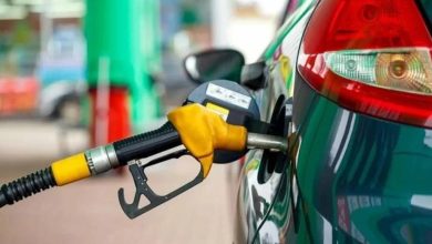 Close-up of a yellow gas nozzle inserted into a green car's fuel tank at a gas station.