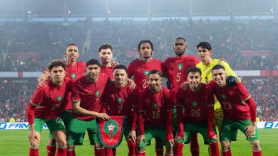 Morocco national football team posing for a group photo on the field with a shield banner in front of a crowded stadium