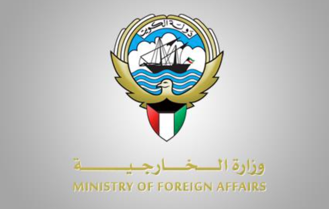 Logo of the Ministry of Foreign Affairs with a ship in a blue circle, waves, and a dove, plus a shield colored like the Kuwaiti flag and Arabic text (ministry seal).