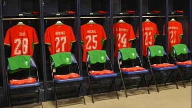 vis_0607202618264718 | MCG24 | موقع إلكتروني مغربي شامل متجدد على مدار الساعة Row of navy lockers with red football jerseys and numbers 28, 27, 25, 24, 23; green duffel bags on chairs in front of each locker.