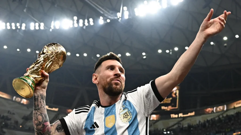 515458 | MCG24 | موقع إلكتروني مغربي شامل متجدد على مدار الساعة Messi in Argentina jersey raises his arm, holding the FIFA World Cup trophy in celebration on a stadium stage