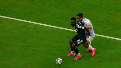 vis_0616202606470515 | MCG24 | موقع إلكتروني مغربي شامل متجدد على مدار الساعة Two soccer players chase the ball on a green pitch, one in dark kit with pink cleats and the other in a light kit close behind near a white line.