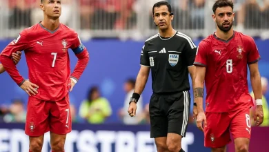 vis_0617202620134388 | MCG24 | موقع إلكتروني مغربي شامل متجدد على مدار الساعة Two Portugal soccer players in red uniforms with numbers 7 and 8 stand beside a FIFA referee on a soccer field.