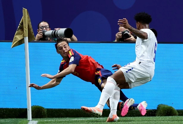 515154548 | MCG24 | موقع إلكتروني مغربي شامل متجدد على مدار الساعة Soccer scene near the corner flag with a red-and-blue jersey player sliding while a white-kit player challenges from the right as photographers watch in the background