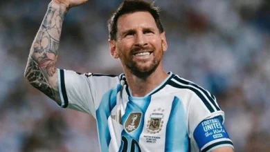 vis_0622202620180715 | MCG24 | موقع إلكتروني مغربي شامل متجدد على مدار الساعة Argentine footballer celebrating on the pitch, fist raised, wearing white-and-light-blue striped jersey with the number 10 and captain armband highlight tattoos on his arm.