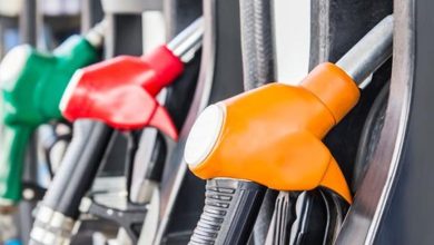 Close-up of colorful fuel nozzles at a gas pump, with an orange nozzle in the foreground and red and green ones blurred in the background.