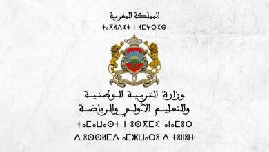 vis_1029202121394269 | MCG24 | موقع إلكتروني مغربي شامل متجدد على مدار الساعة Morocco's coat of arms: two golden lions support a shield with a green pentagram, crown above, on a light textured background with Arabic text above and below.