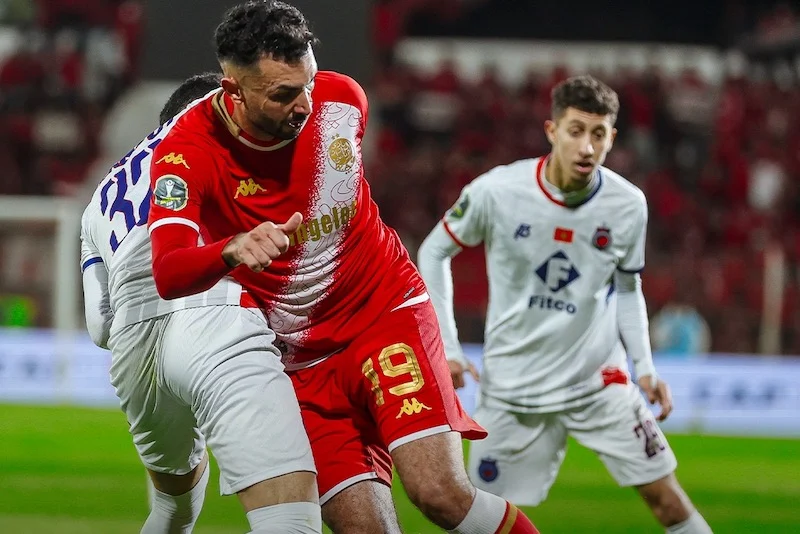wac-ocs1 | MCG24 | موقع إلكتروني مغربي شامل متجدد على مدار الساعة Red jersey player (#19) battles for the ball with a white-jersey defender during a soccer match on a stadium field.