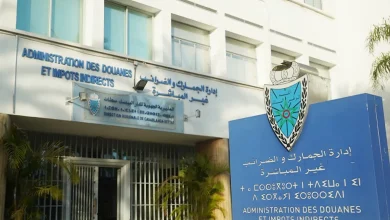 ادارة-الجمارك-والضرائب-غير-المباشرة | MCG24 | موقع إلكتروني مغربي شامل متجدد على مدار الساعة Front of a government office with blue bilingual signs and a crest, doors and white building façade behind palm plants