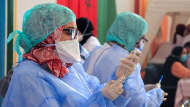 Healthcare workers in blue protective gowns, masks, and hair coverings in a clinical setting.