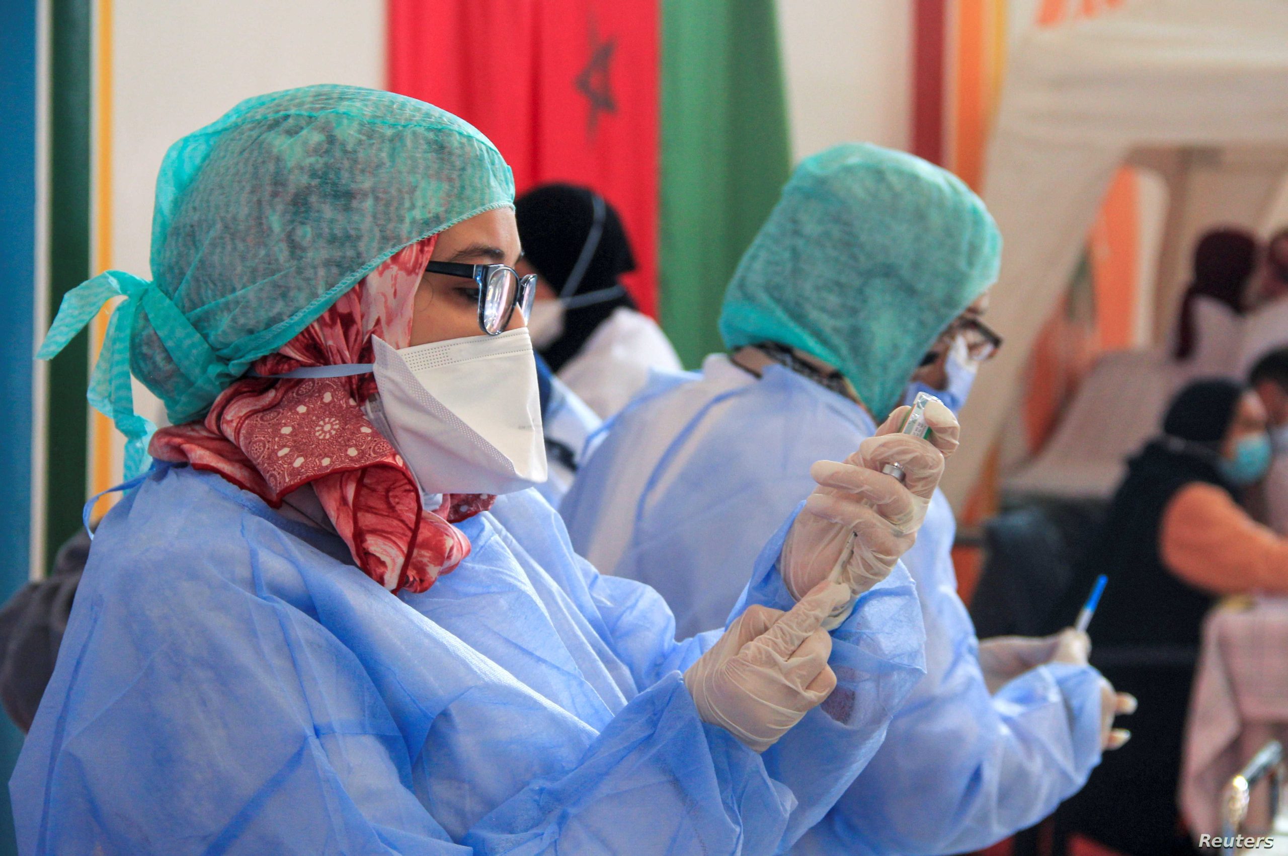 Healthcare workers prepare the COVID-19 vaccines during a national coronavirus vaccination campaign in Sale | MCG24 | موقع إلكتروني مغربي شامل متجدد على مدار الساعة Healthcare workers in blue protective gowns, masks, and hair coverings in a clinical setting.