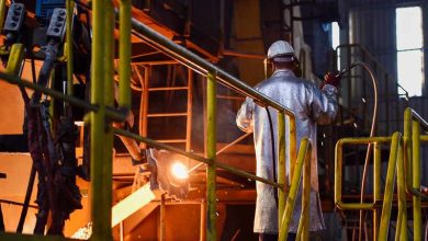 صناعة-تحويلية | MCG24 | موقع إلكتروني مغربي شامل متجدد على مدار الساعة Worker in protective gear welds metal on an industrial line; sparks fly near orange-lit machinery and yellow safety rails.