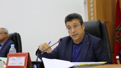عبد السلام البقالي عمدة فاس | MCG24 | موقع إلكتروني مغربي شامل متجدد على مدار الساعة Man in a navy suit and glasses speaking into a microphone at a formal meeting, with papers on the table in front of him and a red nameplate nearby.