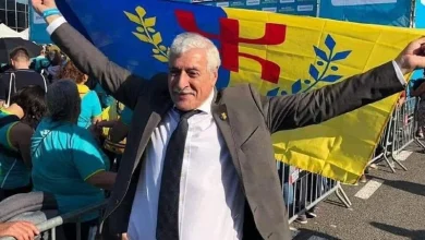 فرحات مهني | MCG24 | موقع إلكتروني مغربي شامل متجدد على مدار الساعة Older man in a suit with arms raised in celebration at a political rally, yellow and blue banner behind him-to the left and right.