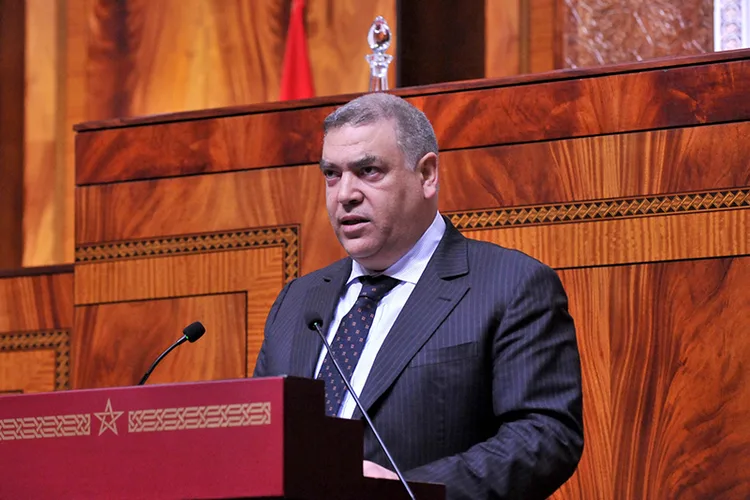 لفتيت-202205 | MCG24 | موقع إلكتروني مغربي شامل متجدد على مدار الساعة Man in a dark suit giving a speech at a wooden podium in a formal assembly hall.**